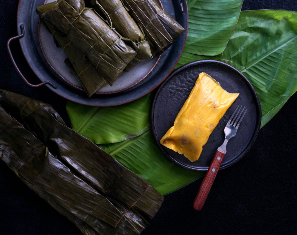 This sweet dessert consists of cornmeal, grated plantain, sweet potatoes, spices and sugar wrapped in steamed banana leaves. Photo by Julia Bognanova/Shutterstock.com