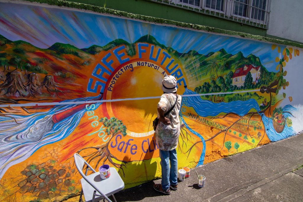 Carol Sorhaindo of the Waitukubuli Artist Association (WAA) painting the CREAD mural in Picard, Dominica, 2022. Photo courtesy Waitukubuli Artist Association