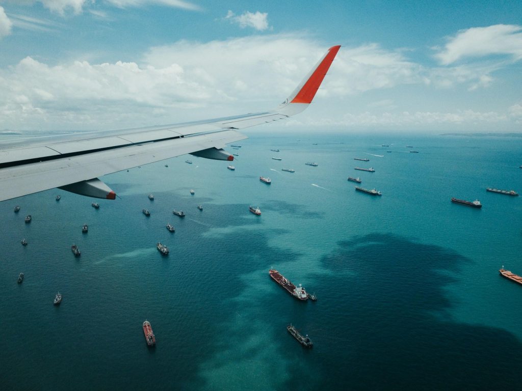 White and red airplane in the sky with the body of water beneath it